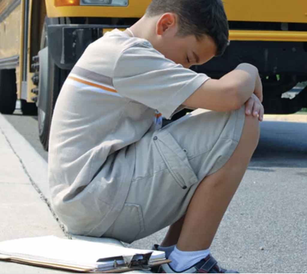 An anxious teen sitting alone beside a school bus, representing teen anxiety counseling in Vancouver.